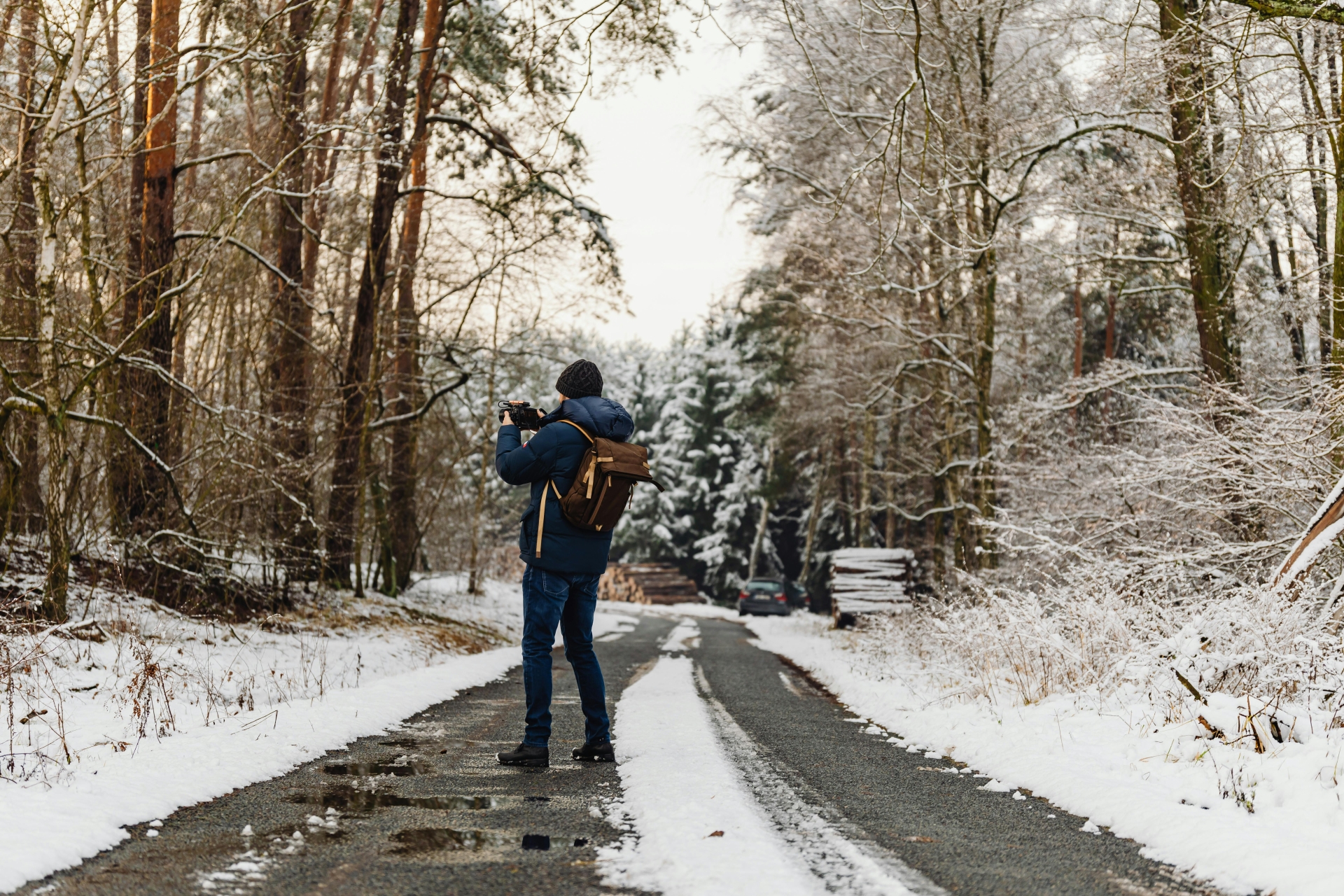 Winterwanderung im Westerwald nahe Schloss Montabaur Person steht auf einem schmalen Waldweg, umgeben von verschneiten Bäumen, trägt Winterjacke, Mütze und Rucksack, fotografiert die winterliche Landschaft unter hellem Himmel