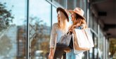 Shopping im Fashion Outlet Center Montabaur Zwei Personen stehen vor einer Glasfassade mit Einkaufstaschen in der Hand, beide tragen helle Kleidung und Hüte, Spiegelungen der Umgebung im Glas