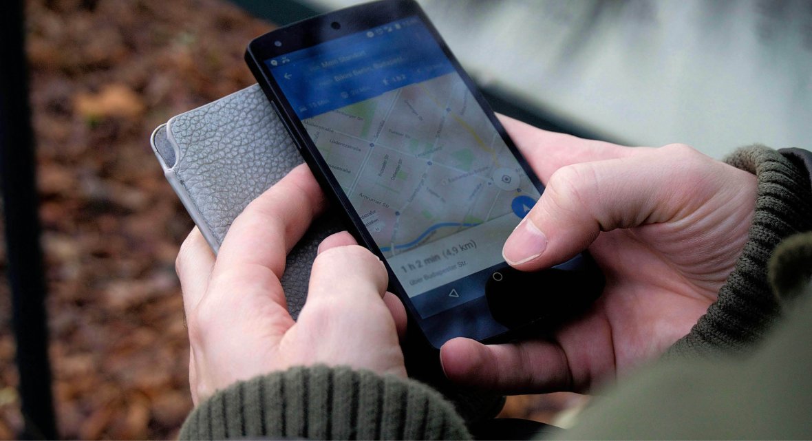 Hände halten Smartphone mit geöffneter Karten-App und unscharfem Herbstlaub im Hintergrund.