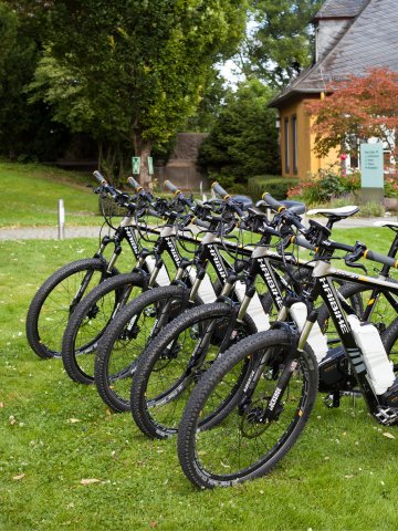 Fünf schwarze E-Bikes der Marke Haibike in einer Reihe auf einer gepflegten Rasenfläche, im Hintergrund ein gelbes Gebäude mit grauem Dach und Bäumen