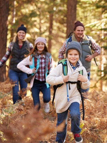 Familienwanderung im Westerwald – mehrere Personen mit Rucksäcken auf einem naturbelassenen Waldweg, umgeben von hohen Bäumen und Herbstlaub beim Kurzurlaub im Schloss Montabaur