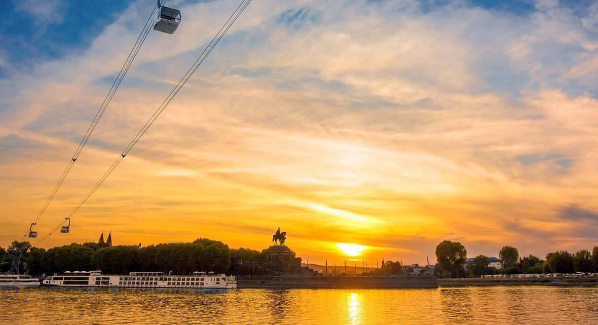 Sunset at the Deutsches Eck in Koblenz Evening scene at the Deutsches Eck in Koblenz – sunset over the Rhine with the equestrian monument, cable cars, and excursion boats, golden reflection on the water