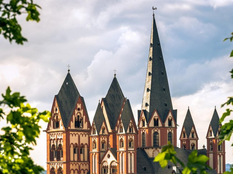 Ausflug zum Limburger Dom – Kultur erleben nahe Schloss Montabaur Limburger Dom – beeindruckende Kathedrale mit rot-weißer Fassade und hohen Türmen, umgeben von grünem Laub, unter leicht bewölktem Himmel beim Ausflug vom Schloss Montabaur