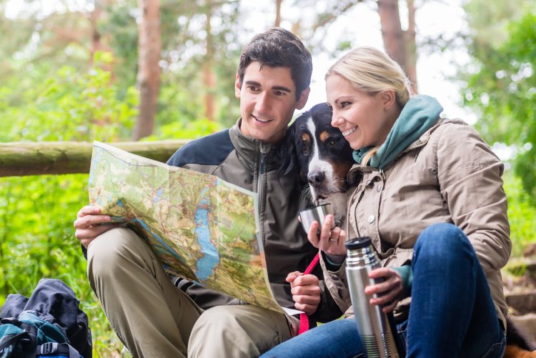 Pause beim Wandern im Westerwald nahe Schloss Montabaur Wandern im Westerwald – zwei Personen sitzen auf einer Holzbank im Wald, studieren eine Wanderkarte und trinken aus einer Thermoskanne, umgeben von grünem Laub und Natur beim Kurzurlaub im Schloss Montabaur