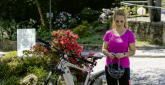E-Bike-Tour rund um Schloss Montabaur Person steht neben einem weißen E-Bike auf einem gepflasterten Weg, hält einen Fahrradhelm in der Hand, umgeben von blühenden Sträuchern und Grünanlagen beim Kurzurlaub im Schloss Montabaur