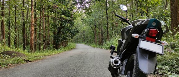 Motorradtour durch den Westerwald nahe Schloss Montabaur Schwarzes Motorrad steht auf einer schmalen Asphaltstraße, die durch einen dichten grünen Wald führt, umgeben von hohen Bäumen und Natur beim Kurzurlaub im Schloss Montabaur