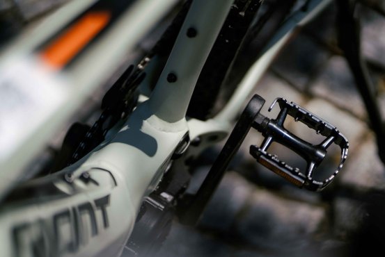 Nahaufnahme eines E-Bike-Pedals und Rahmens mit klar sichtbarer Kettenführung, aufgenommen auf einem gepflasterten Untergrund im Sonnenlicht