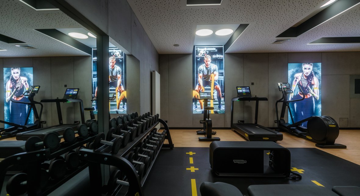 Premium-Fitnessbereich – Hotel Schloss Montabaur Fitnessbereich im Hotel Schloss Montabaur mit Laufbändern, Hantelbank, Spiegelwand und digitalen Displays.
