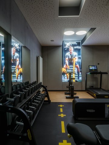 Fitnessbereich im Hotel Schloss Montabaur mit Laufbändern, Hantelbank, Spiegelwand und digitalen Displays.