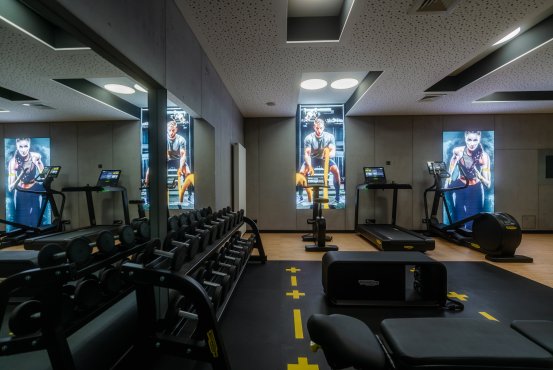 Fitnessbereich im Hotel Schloss Montabaur mit Laufbändern, Hantelbank, Spiegelwand und digitalen Displays.