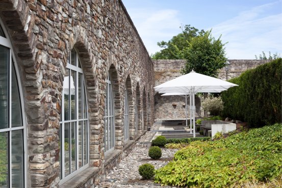 Spa Fresh Air Area – Montabaur Castle Hotel Fresh air spa area at Montabaur Castle Hotel featuring seating, a white umbrella, and a well-maintained garden.